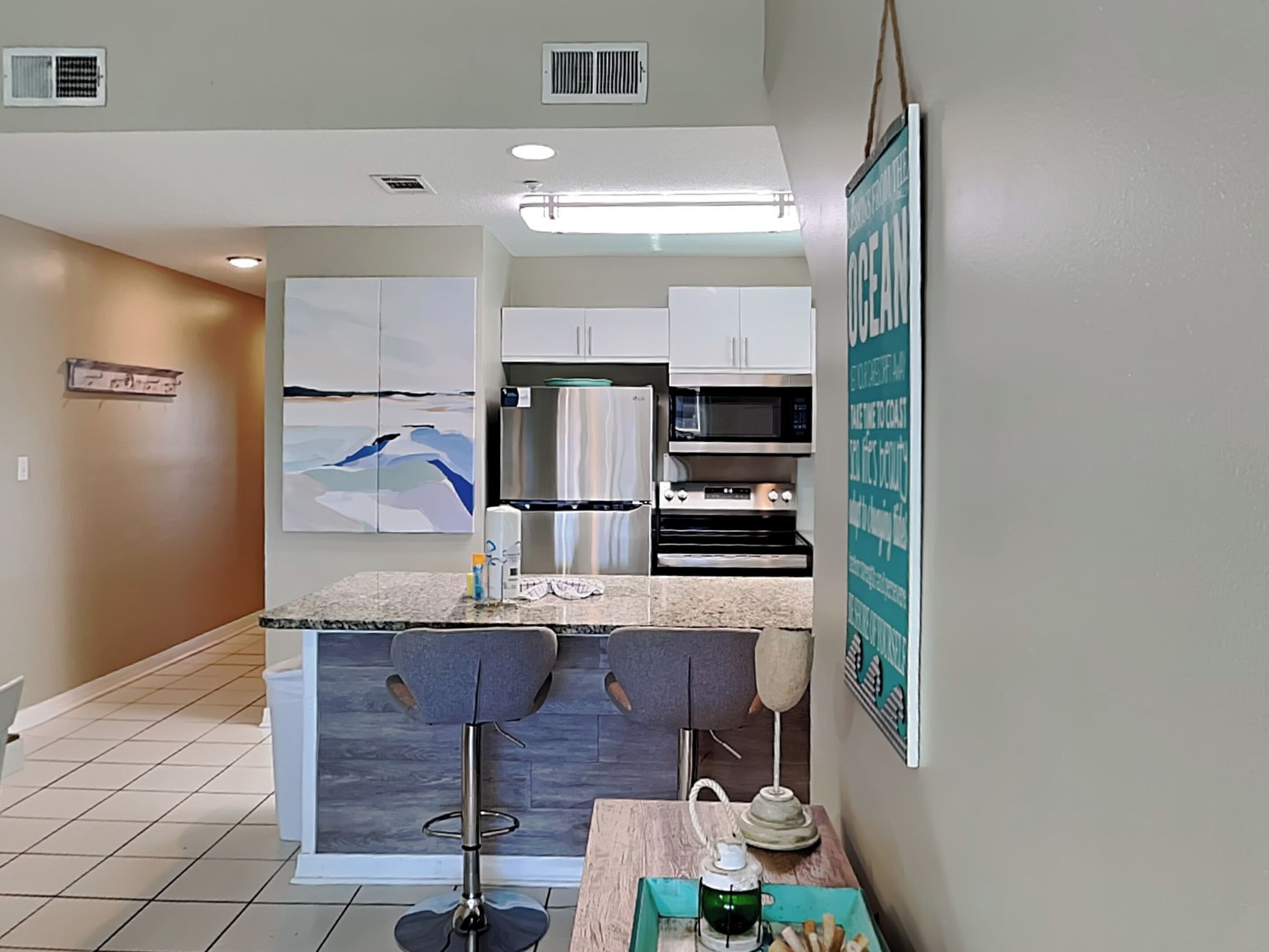 A modern kitchen with a central island, bar stools, a microwave, oven, and a refrigerator.