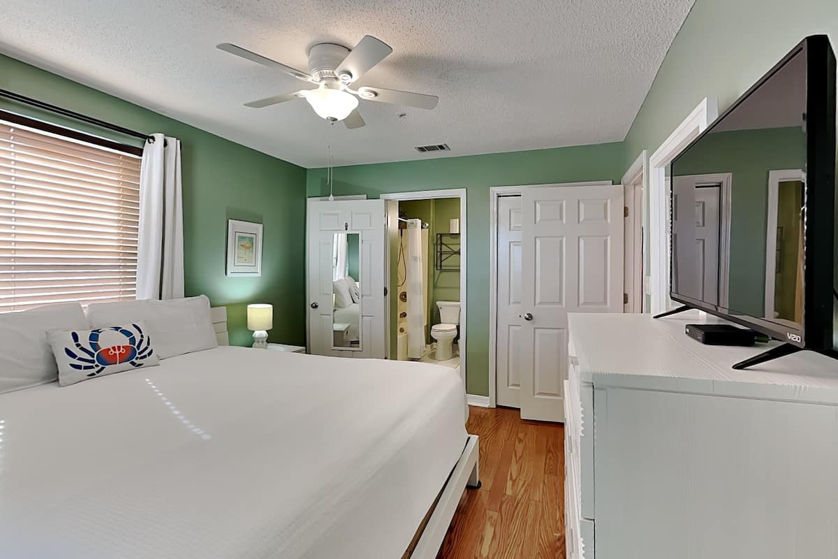 A bedroom with a bed, a ceiling fan, a dresser, a mirror, and a door leading to a bathroom.