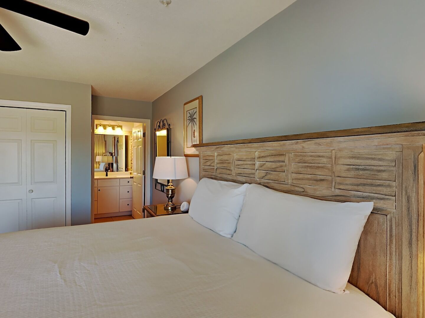 A neatly arranged bedroom with a large bed, a wooden headboard, a bedside table with a lamp, and a mirror.