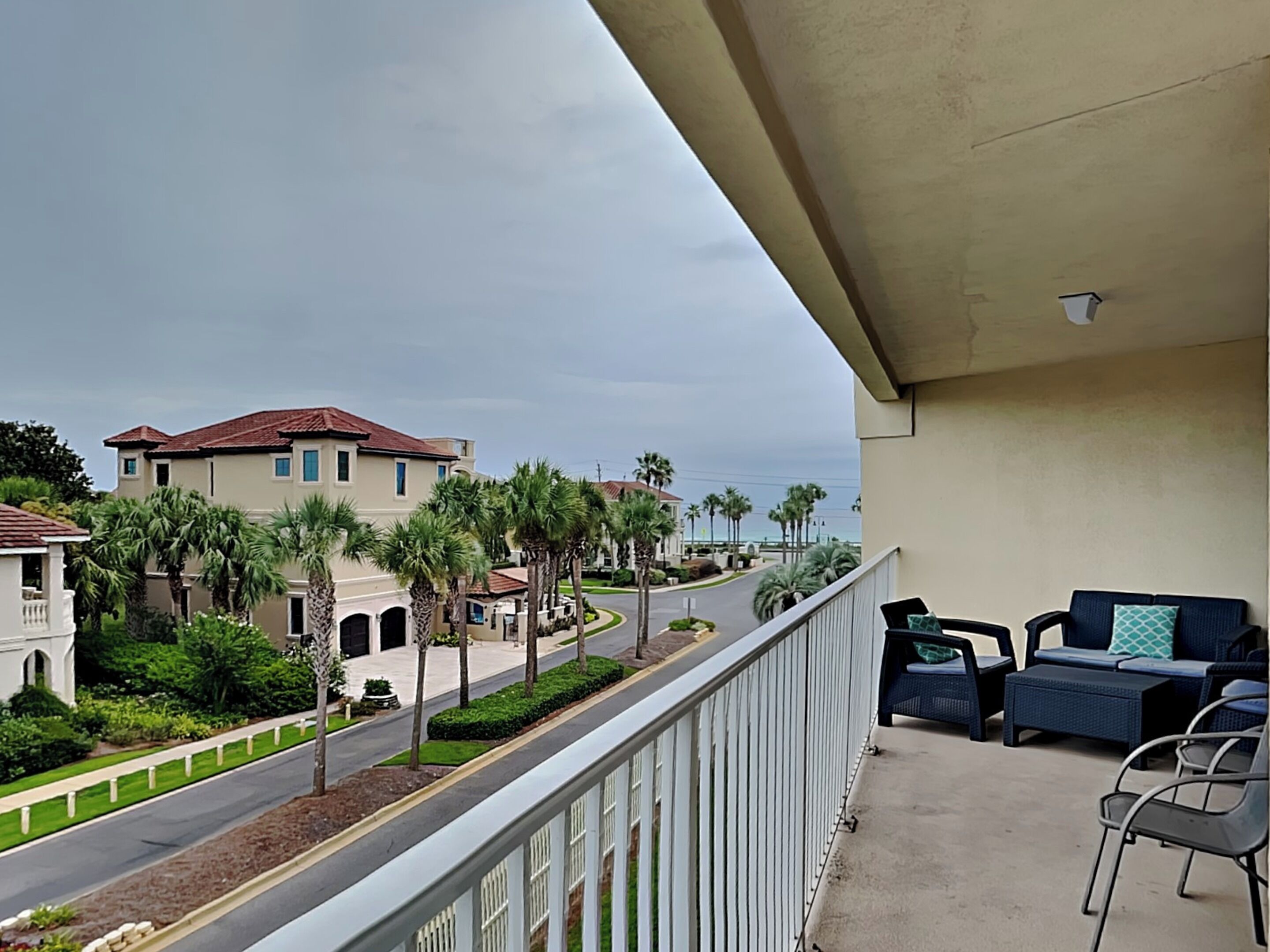 Un balcon aménagé avec du mobilier d’extérieur, donnant sur une rue bordée de palmiers et de maisons.