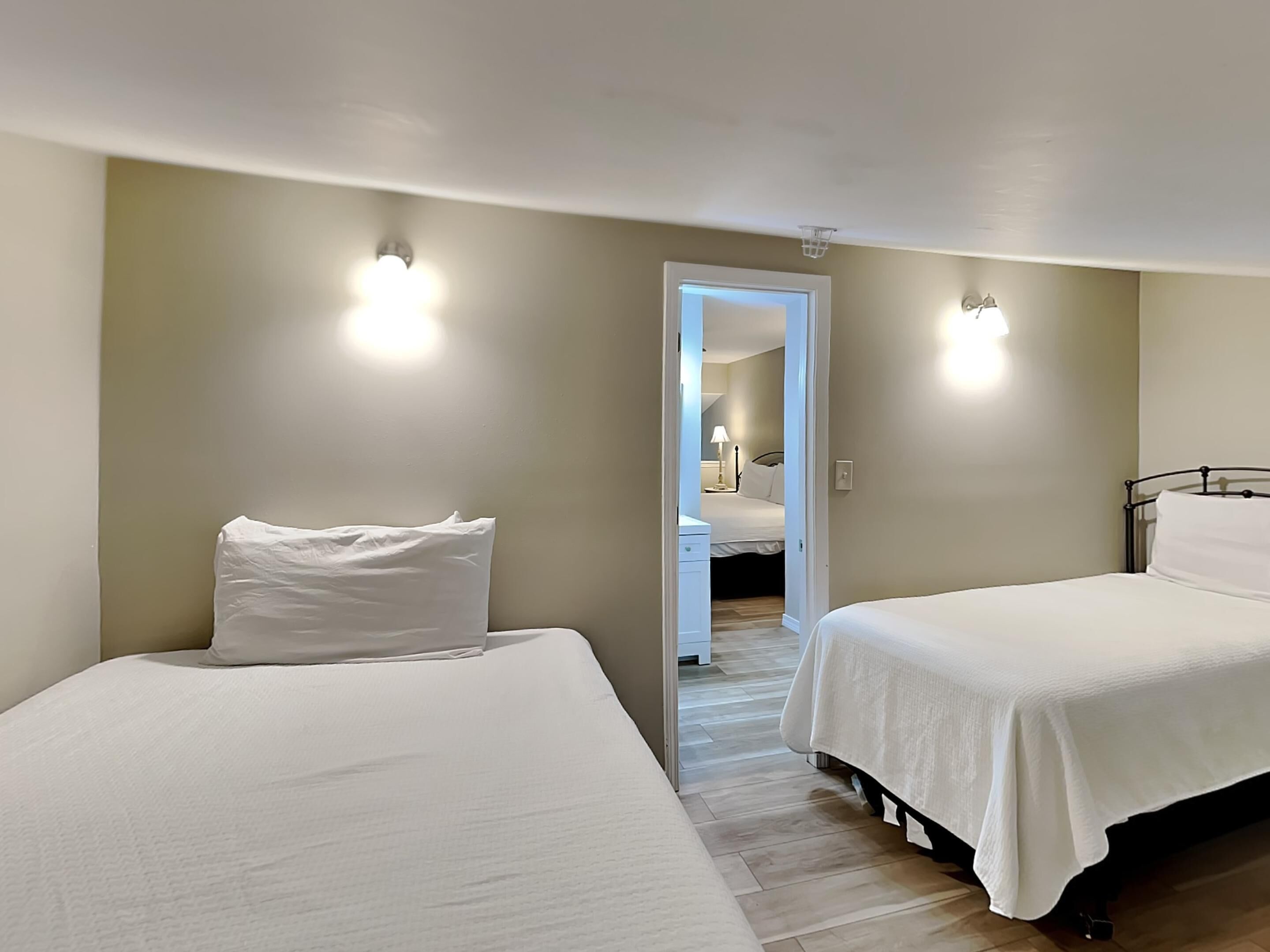 A bedroom with two beds, a wooden floor, and a door leading to another room.