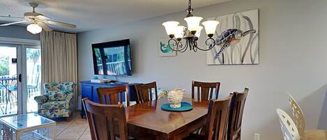 Un coin repas avec une table et des chaises en bois, un lustre, un téléviseur et un tableau représentant une tortue accroché au mur.