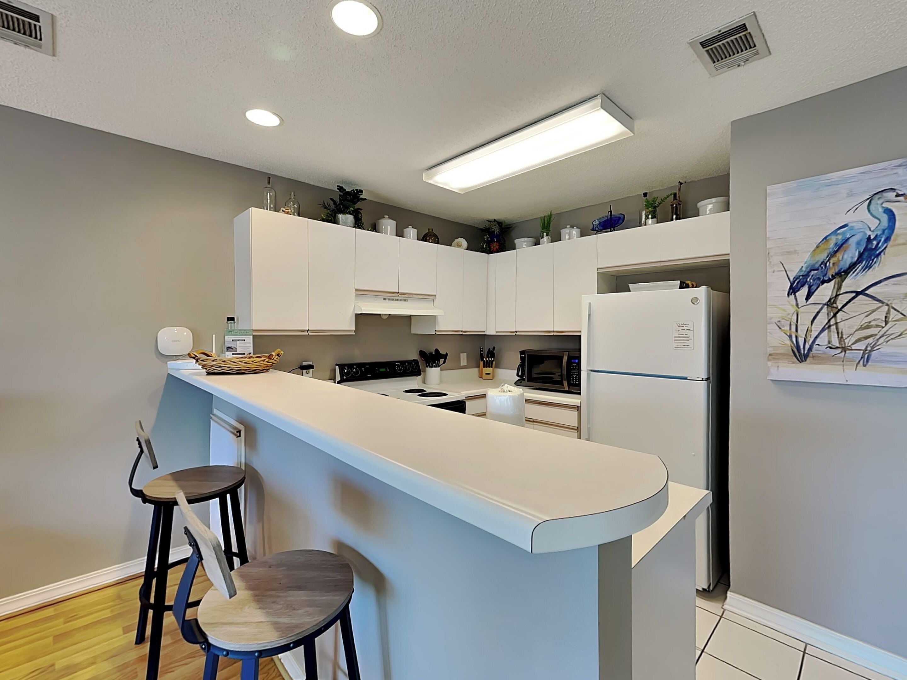 Une cuisine moderne avec des meubles blancs, un îlot central doté de tabourets, un four à micro-ondes et un réfrigérateur.