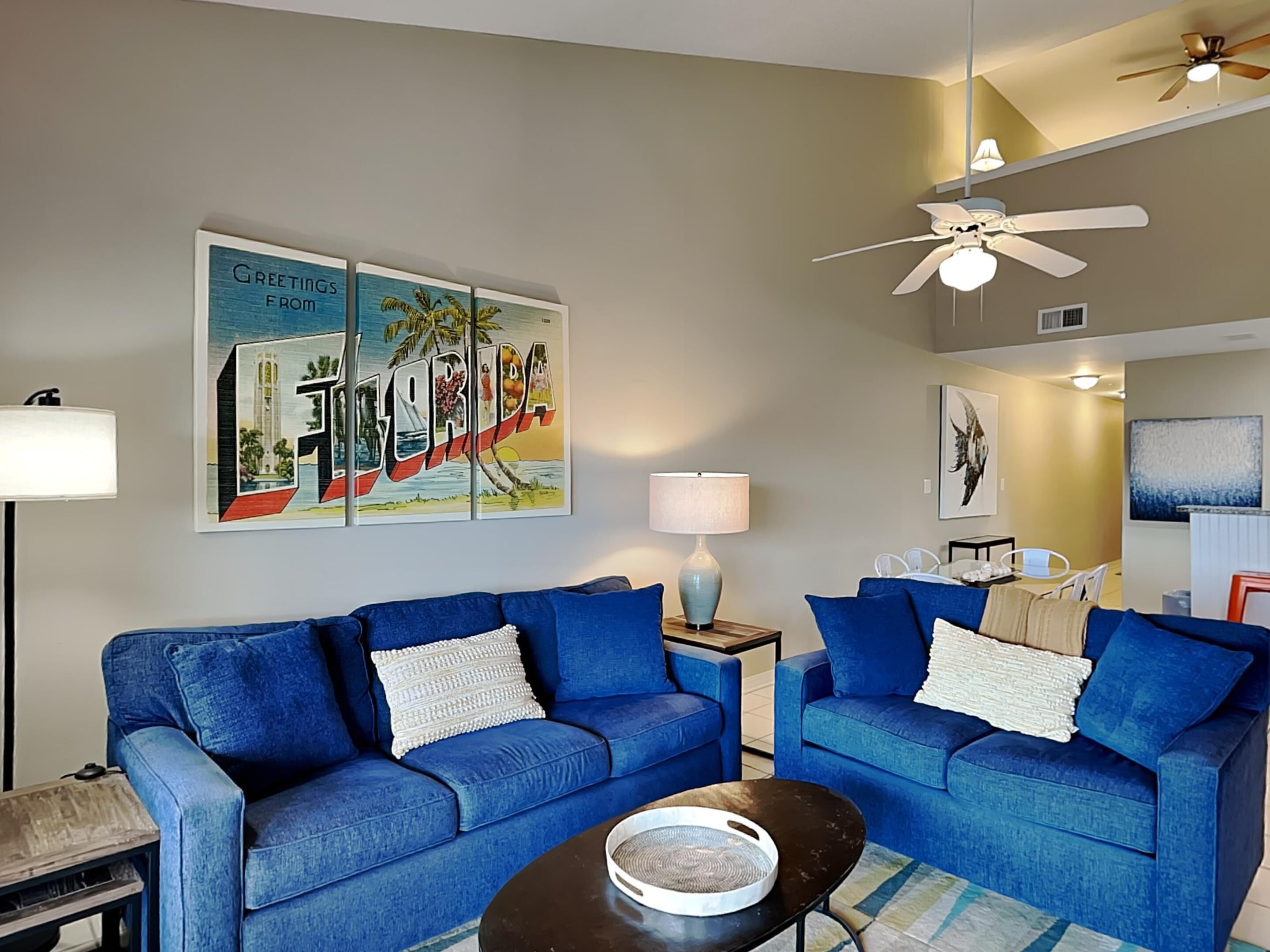 Un salon avec deux canapés bleus, une table basse et un tableau représentant la Floride accroché au mur.