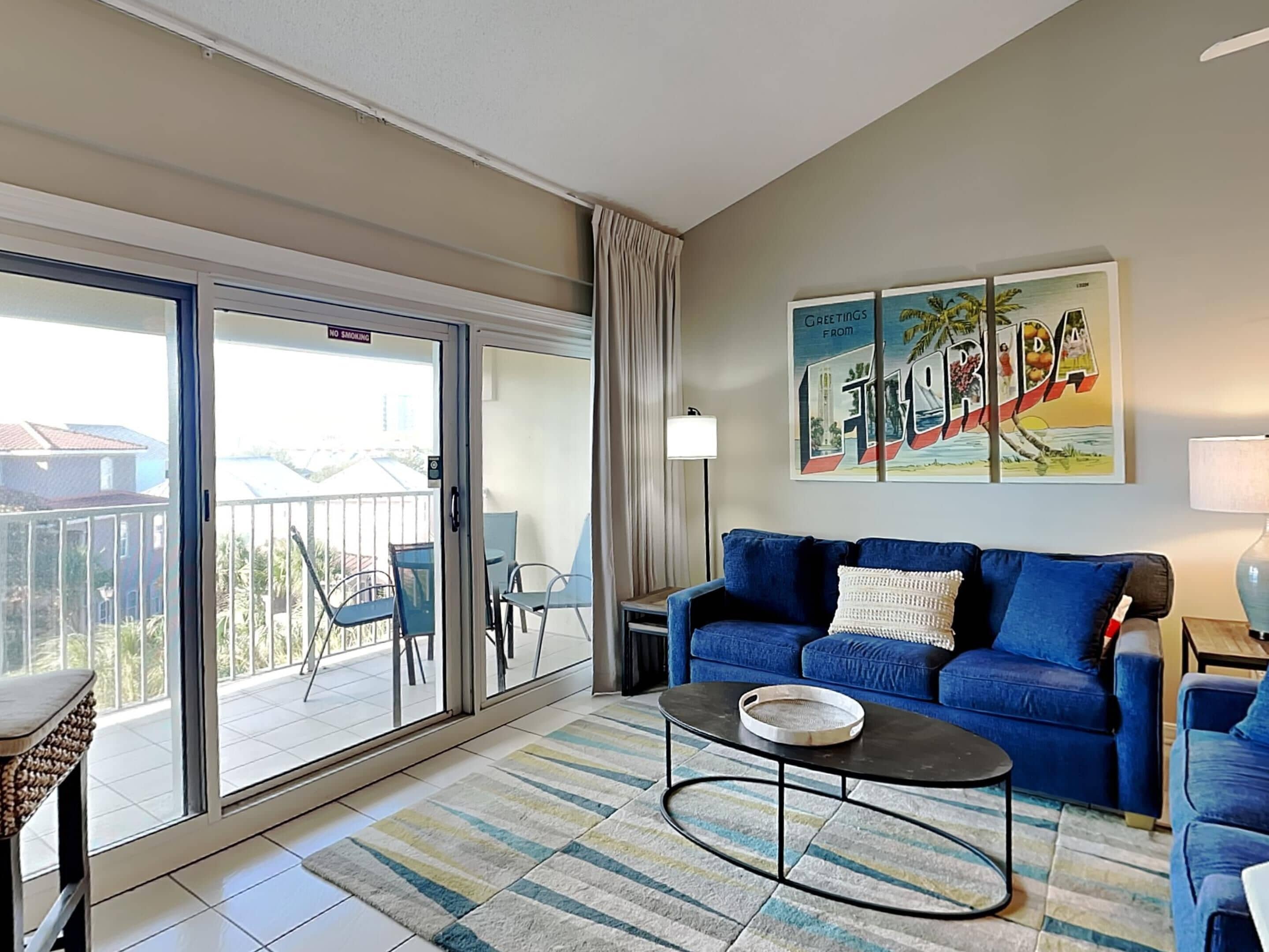 A living room with a blue sofa, a coffee table, and a balcony with chairs.