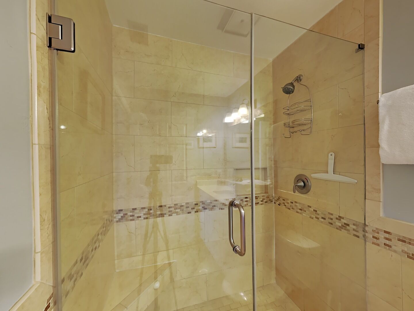 A glass-enclosed shower with a handheld showerhead, a wall-mounted sink, and a towel rack.