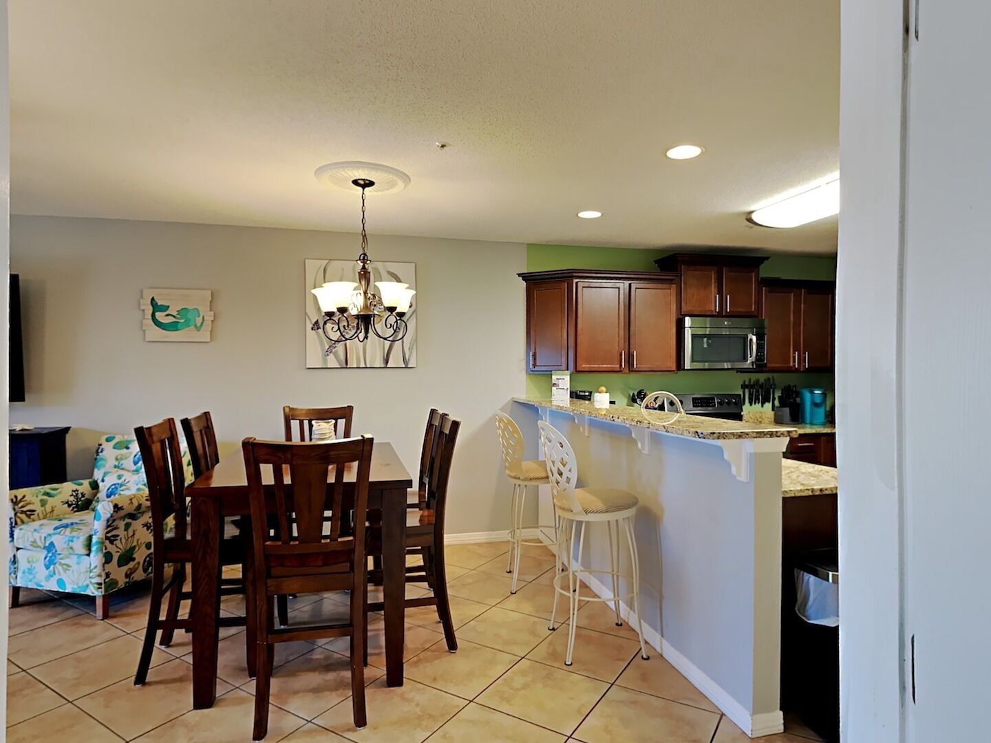 A kitchen with wooden cabinets, a microwave, and a dining area with a chandelier.