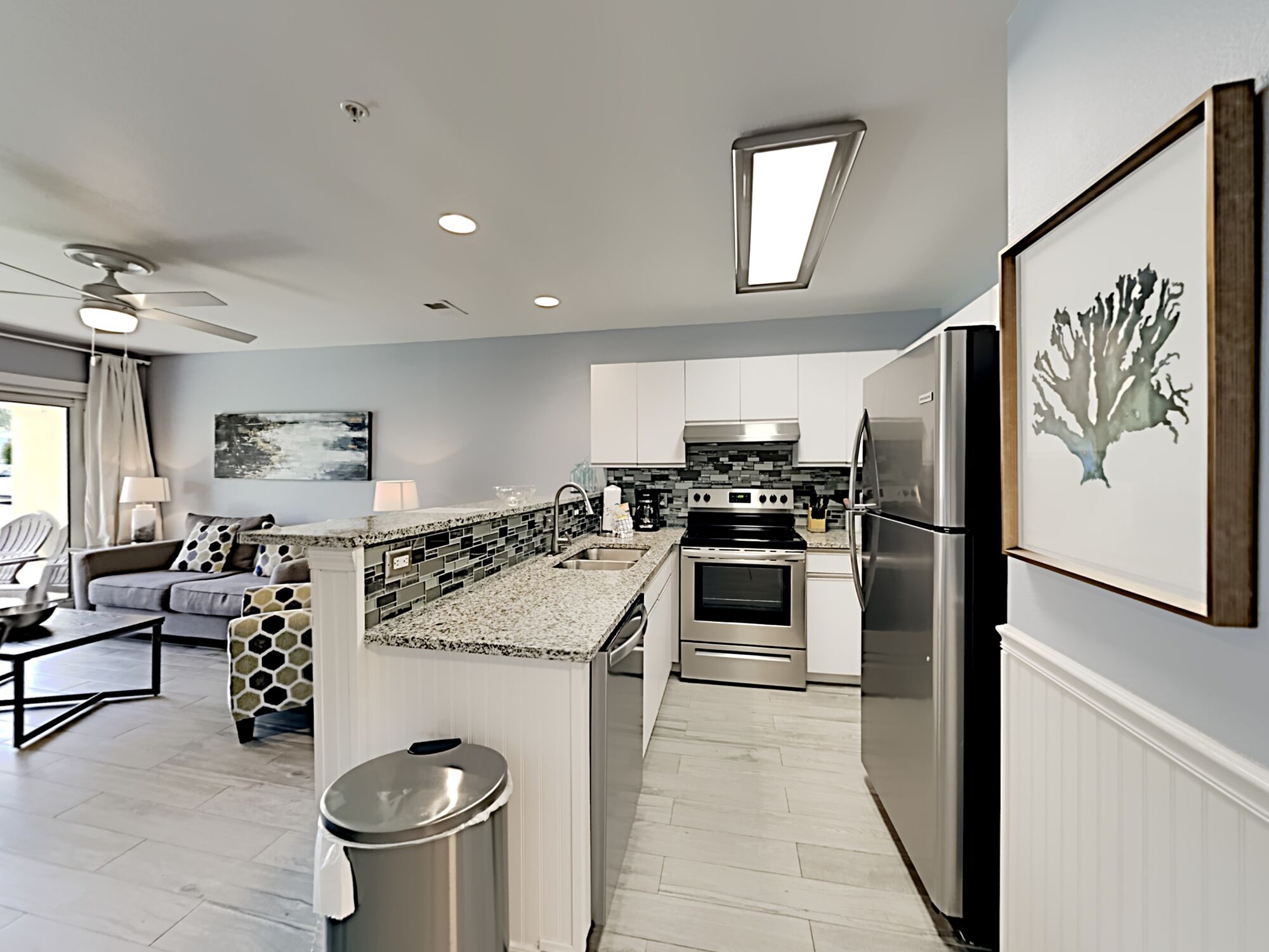 A modern kitchen with a central island, stainless steel appliances, and a dining area with a sofa and table.