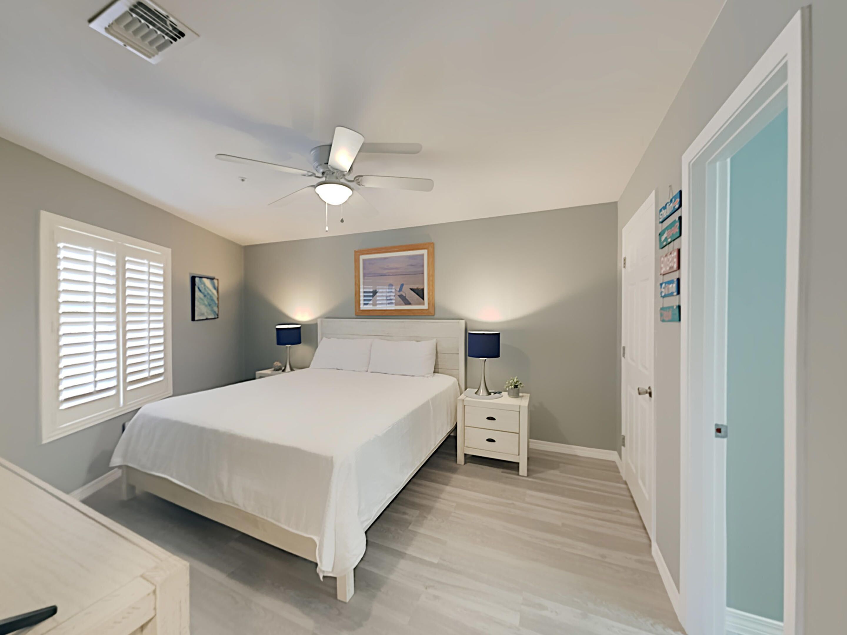 A bedroom with a bed, nightstands, a ceiling fan, and a door.