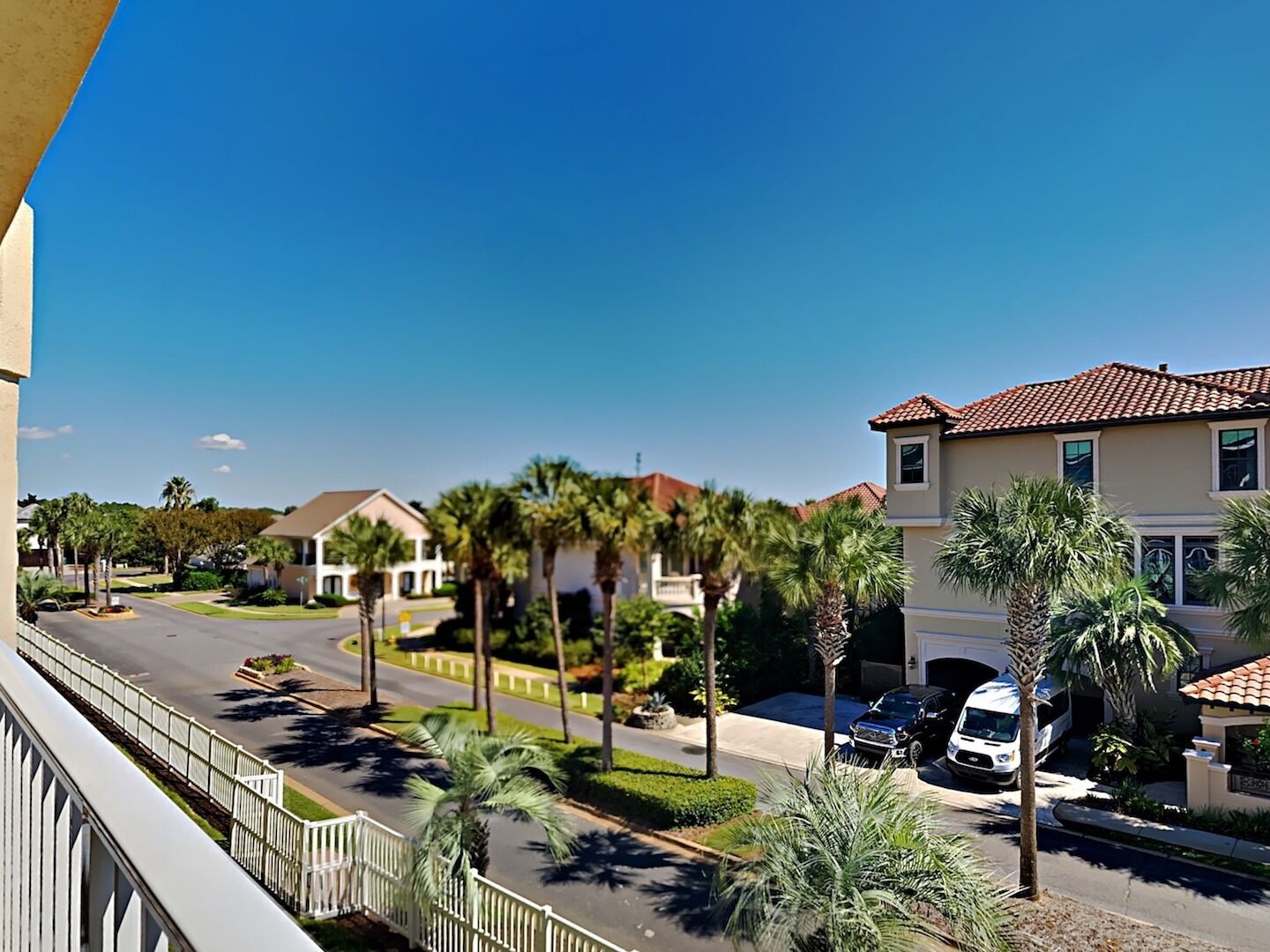 A residential street with houses, palm trees, and a clear blue sky.