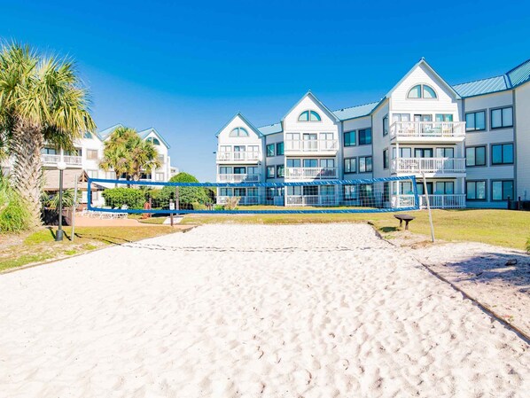 A beachfront hotel with multiple-story buildings, a sandy beach in the foreground, and a clear blue sky.