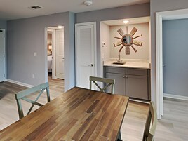 Un comedor con mesa y sillas de madera, una cocina con un ventilador de techo llamativo, y un pasillo que conduce a otra habitación.
