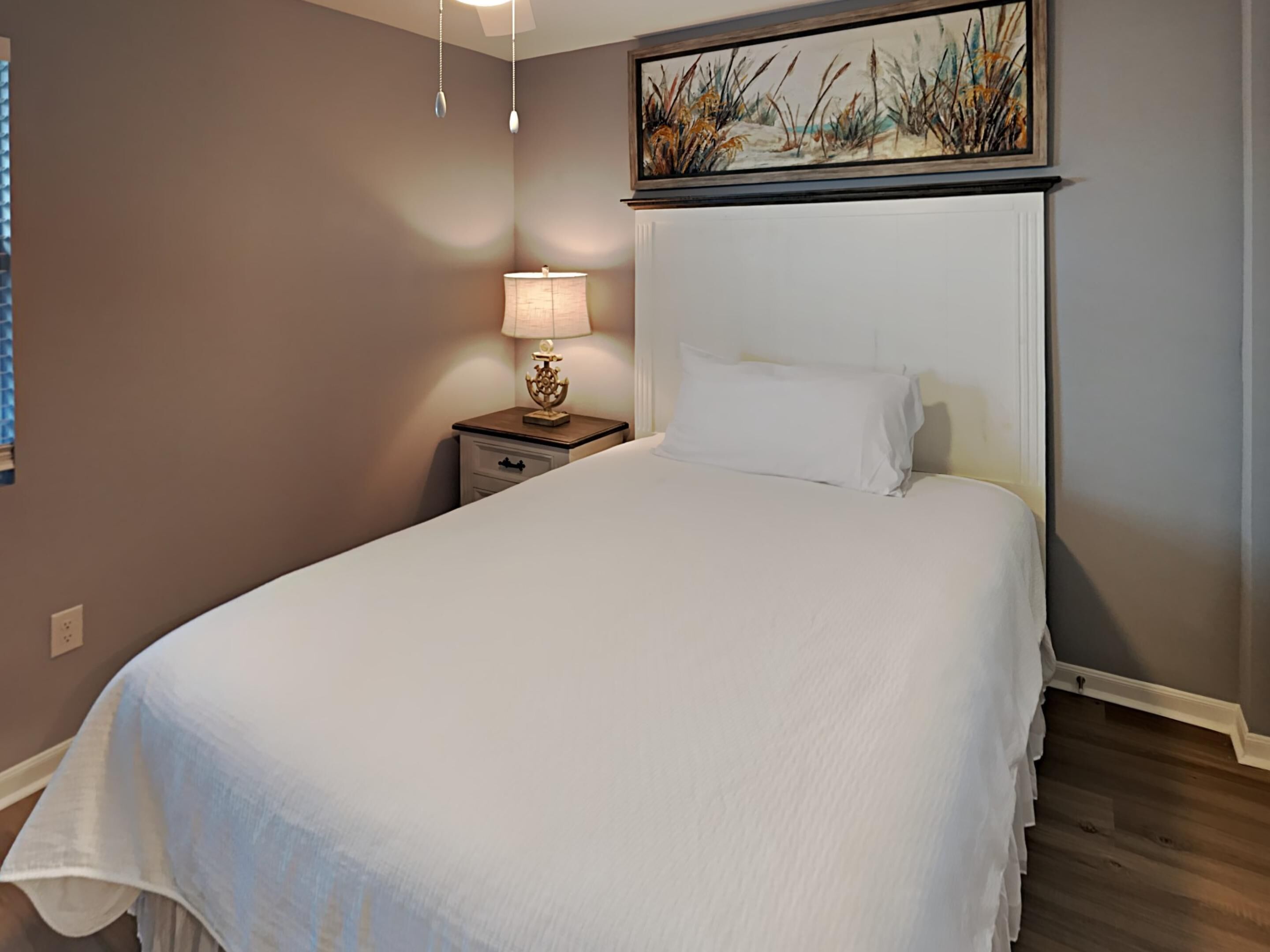 Un letto rifatto con lenzuola bianche, una lampada da comodino e un comodino con un oggetto decorativo.