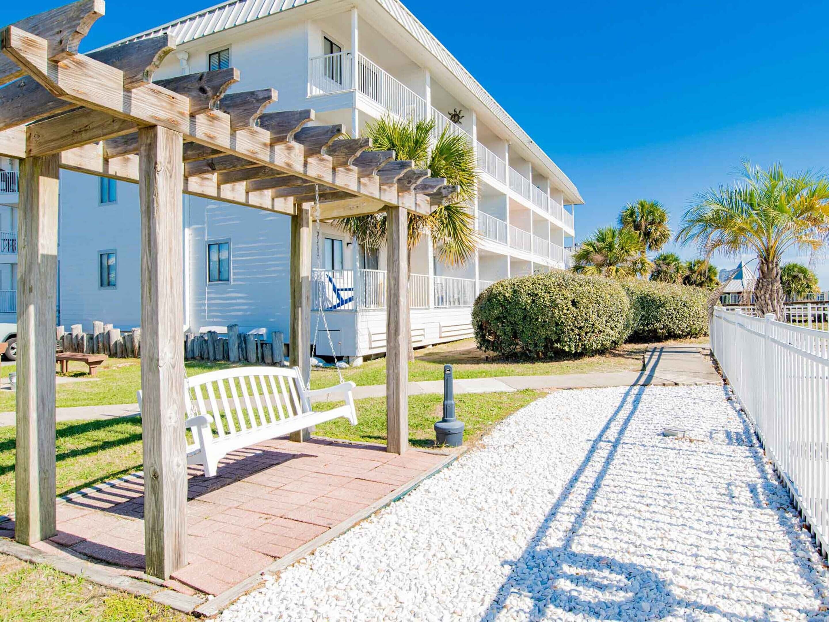 Ein Hotel direkt am Strand mit überdachter Außenbestuhlung, einem Weg zum Gebäude und einem gepflegten Rasen.