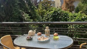 A round table with chairs on a balcony, surrounded by greenery and buildings in the background. - Dream Cottage Nikiti Greece (Sithonia)