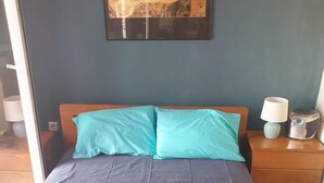 A neatly made bed with a blue and beige bedspread, two pillows, and two folded towels. - Dream Cottage Nikiti Greece (Sithonia)