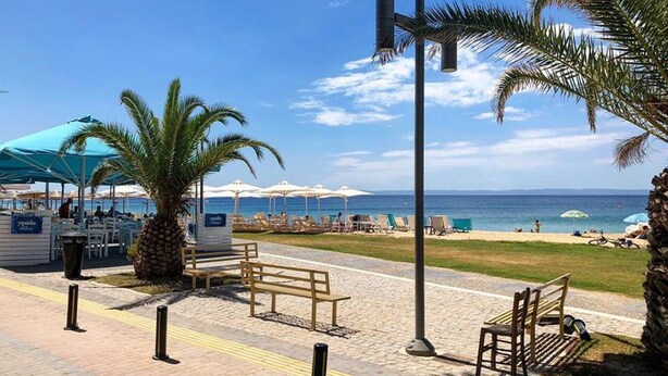 A beachside area with a pathway, benches, umbrellas, and a view of the sea. - Dream Cottage Nikiti Greece (Sithonia)