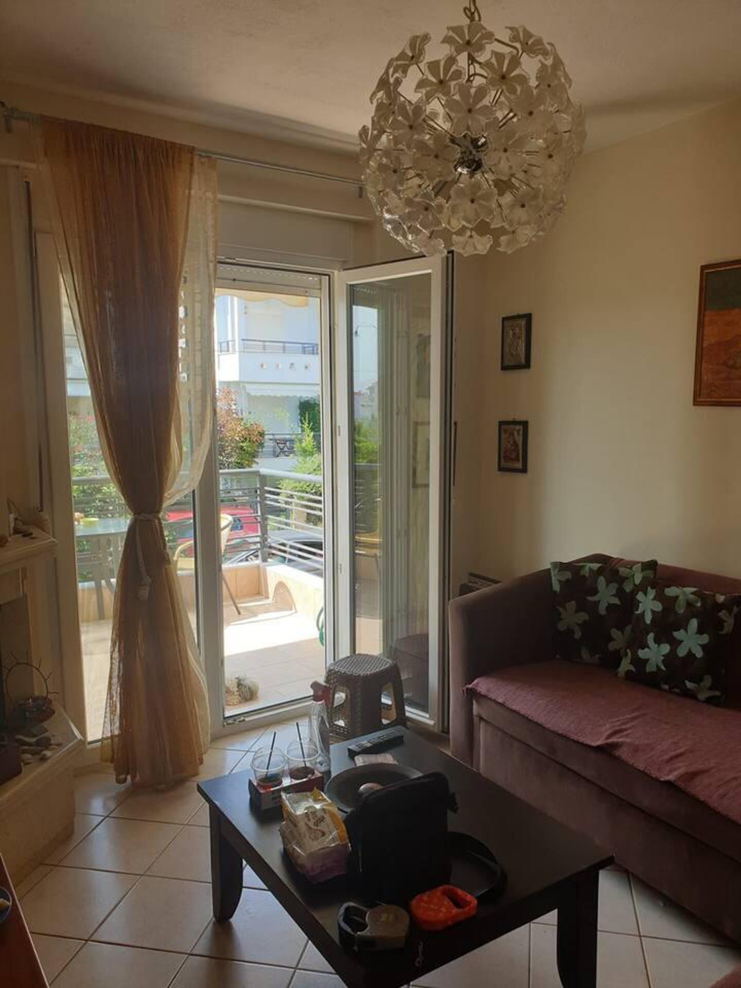 A living room with a sofa, a coffee table, and a chandelier. There is a sliding glass door leading to an outdoor balcony.