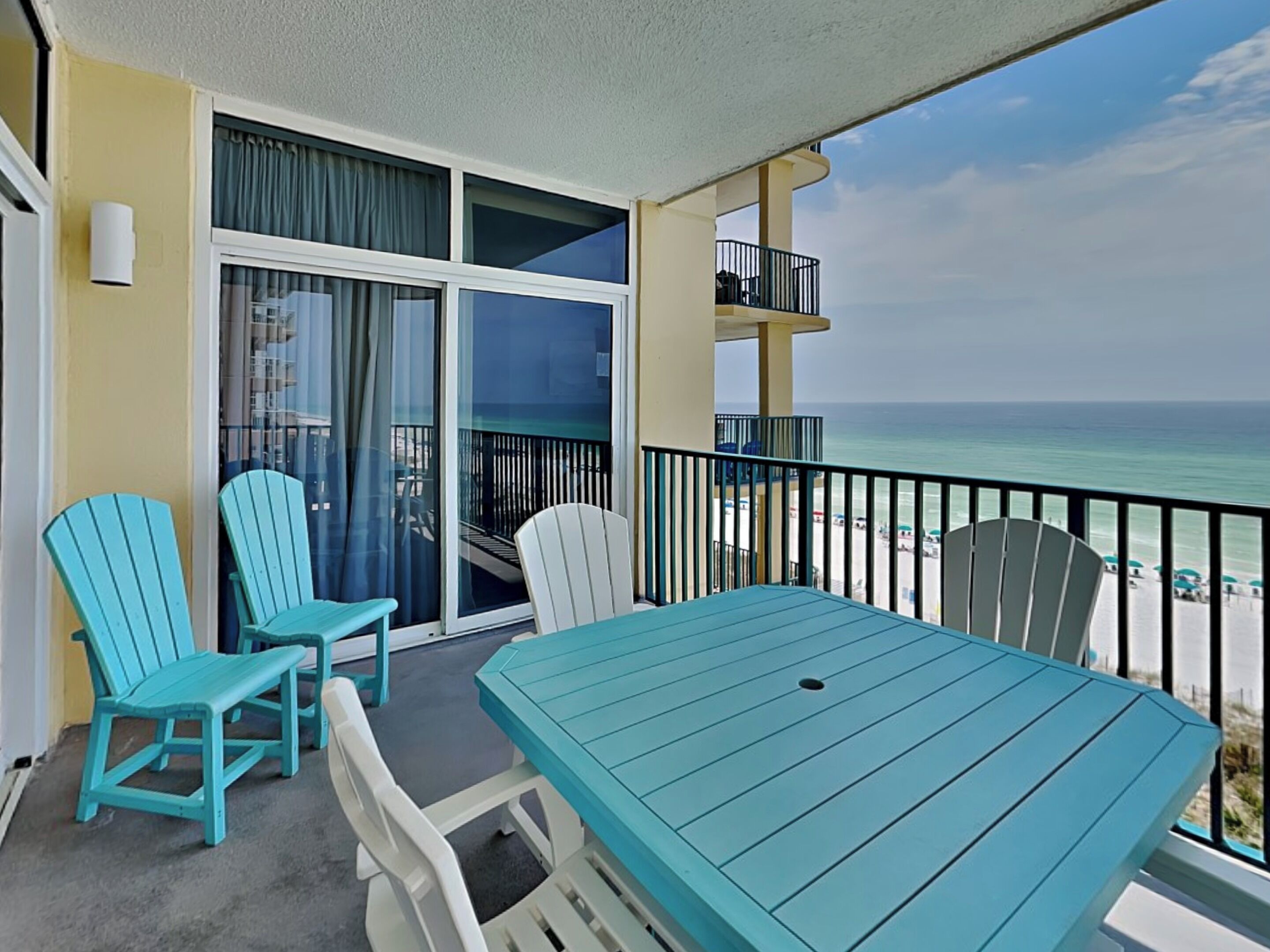 A balcony with a table and chairs, overlooking a beach.
