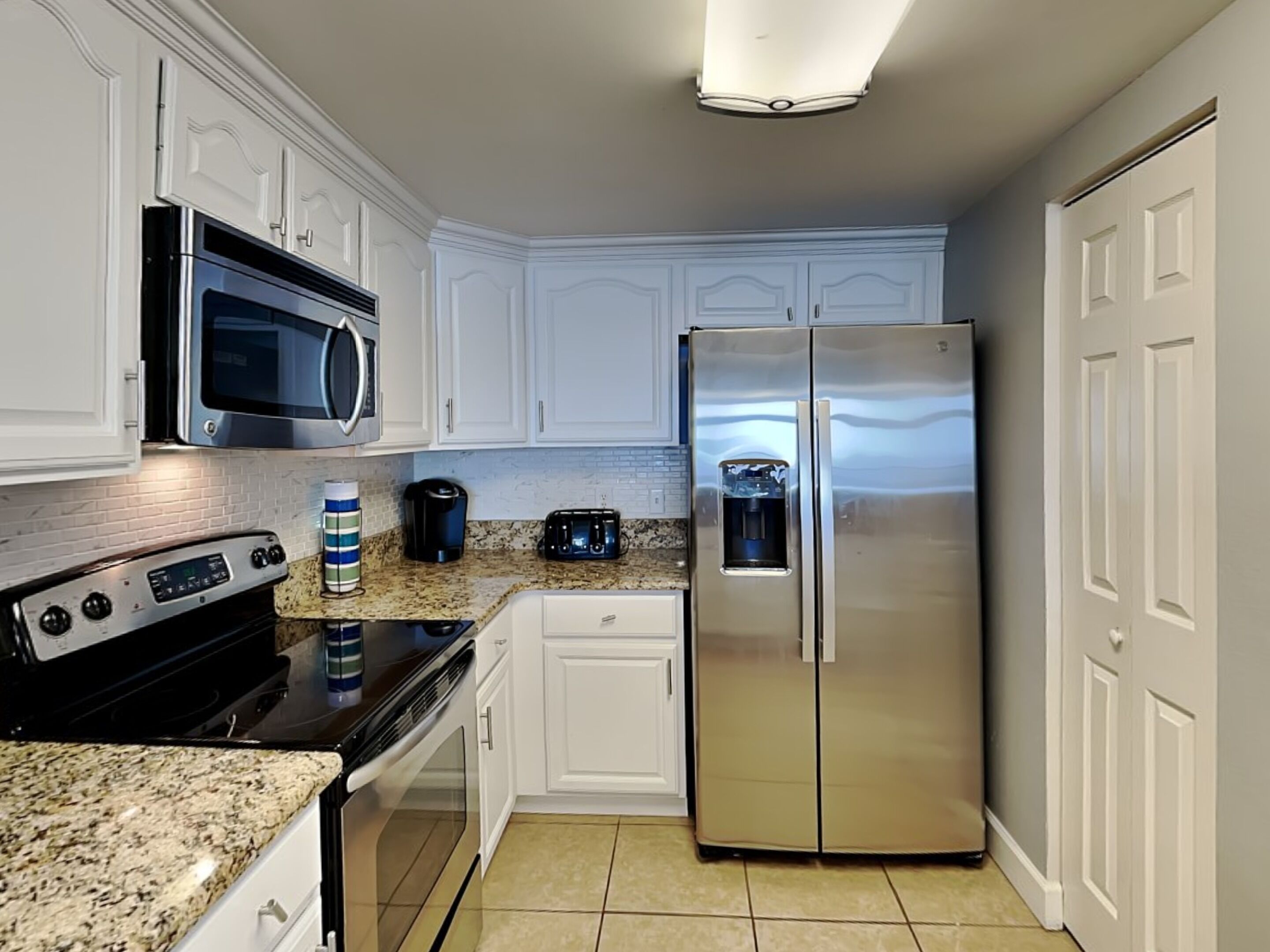 Una cocina con armarios blancos, un refrigerador de acero inoxidable, un microondas, un tostador y una cafetera.