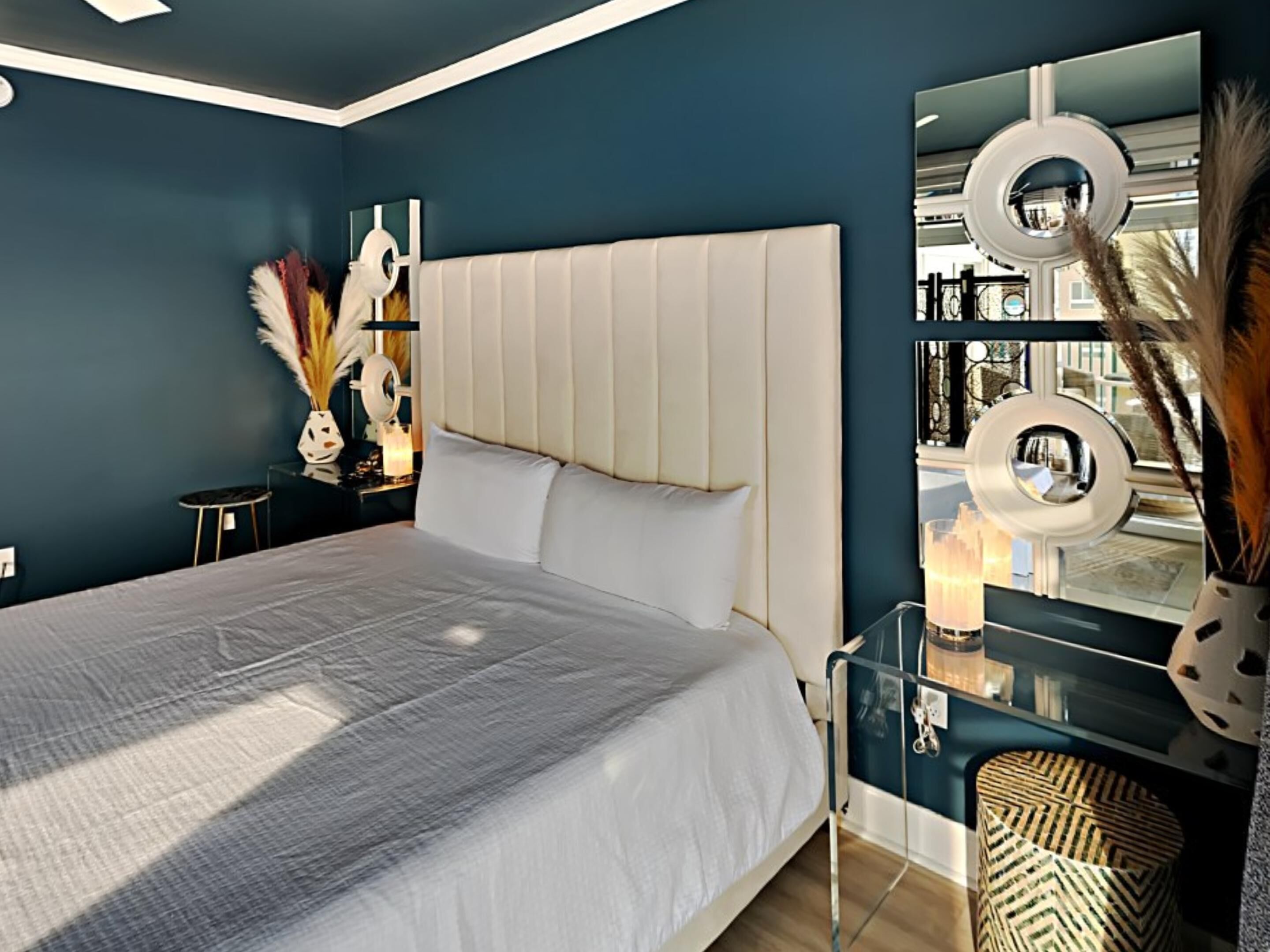 A modern bedroom with a large bed, a bedside table, a mirror, and decorative items.
