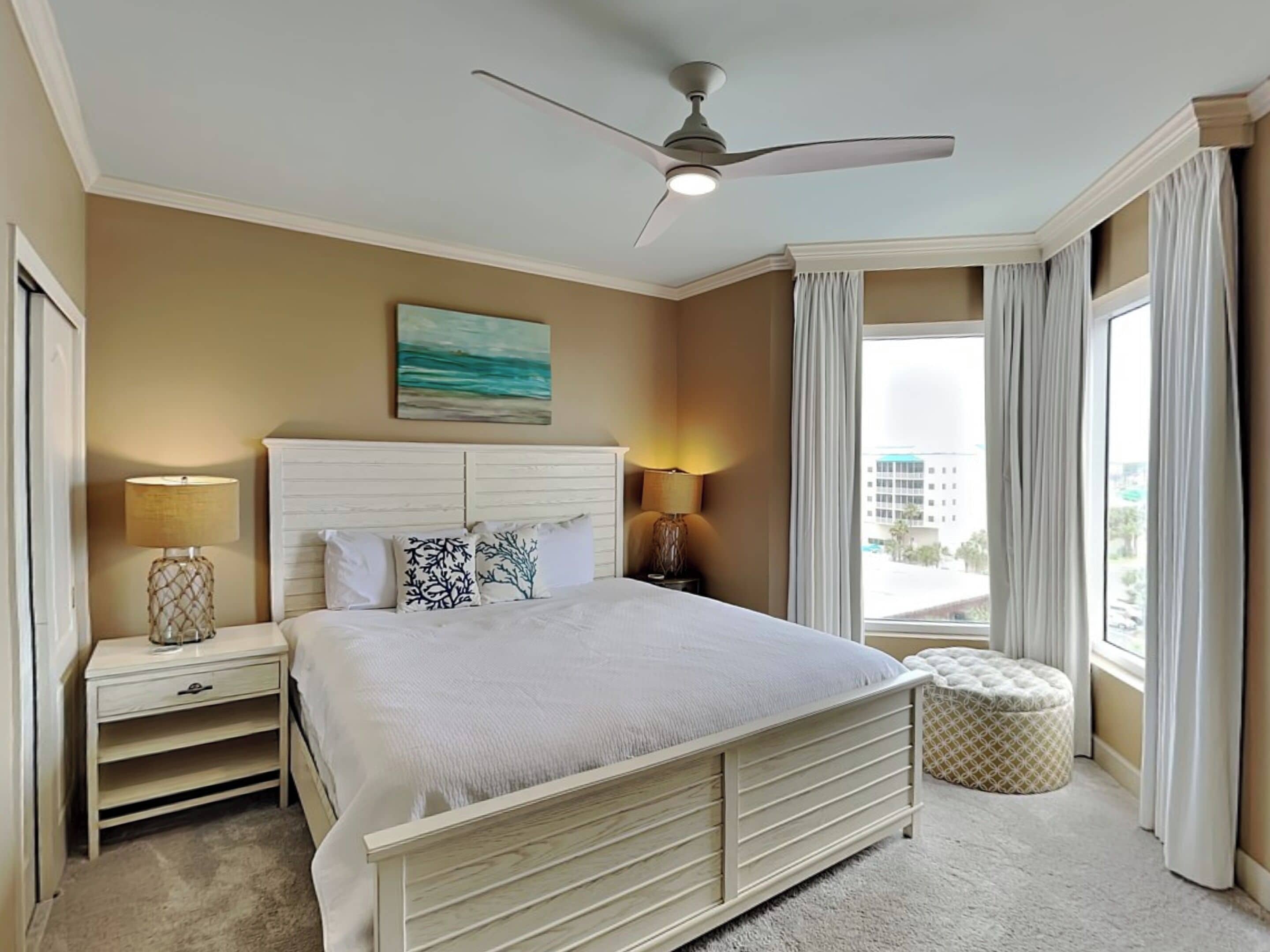 A hotel room with a bed, two bedside tables, a ceiling fan, a window with curtains, and a view of the outside.