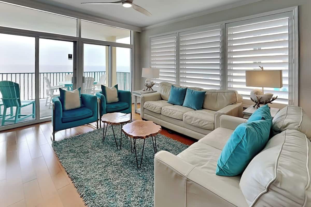 A spacious living room with a balcony, a ceiling fan, and a large window with blinds.