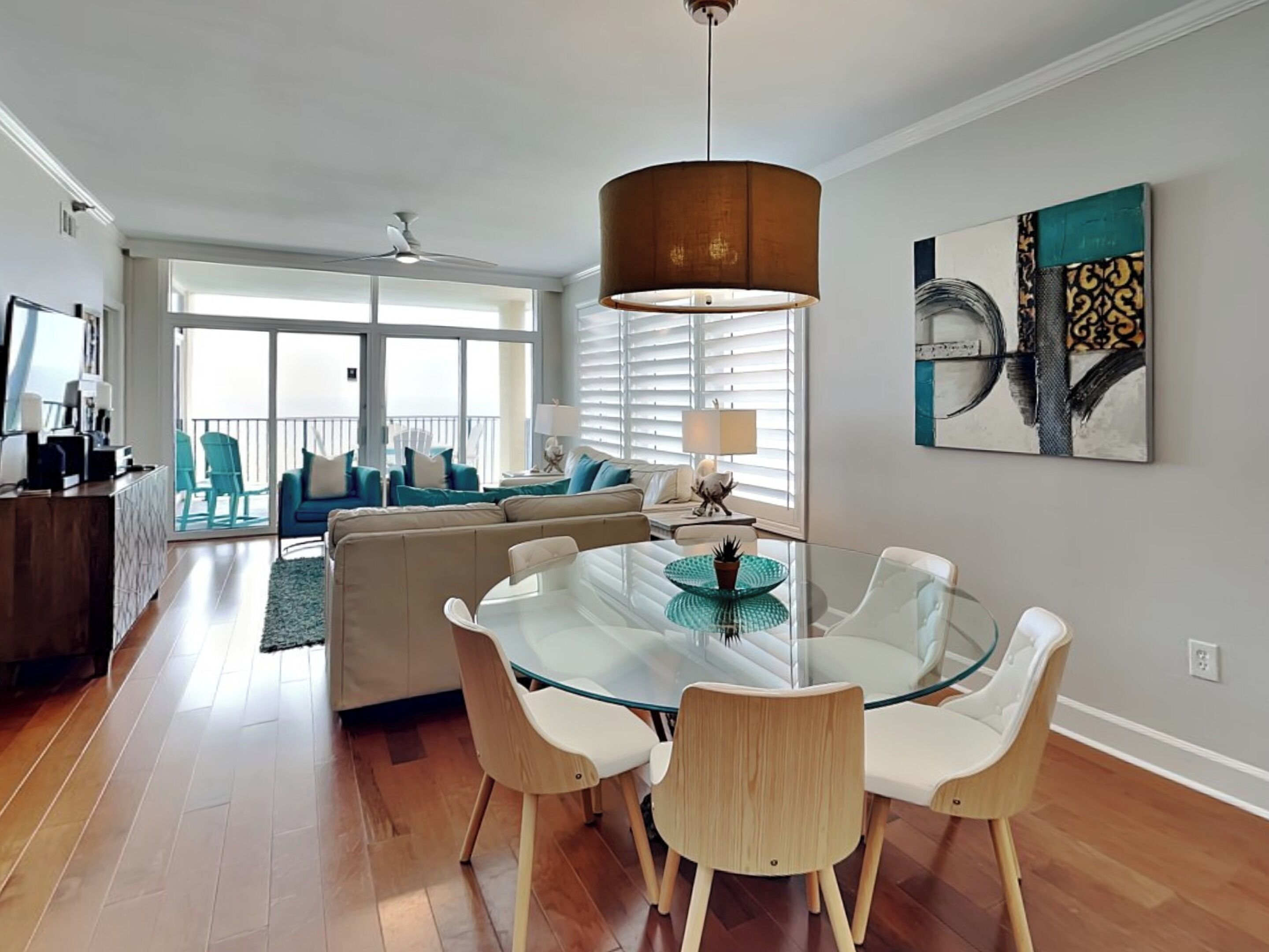 A modern living room with a glass dining table, beige sofa, and teal chairs.