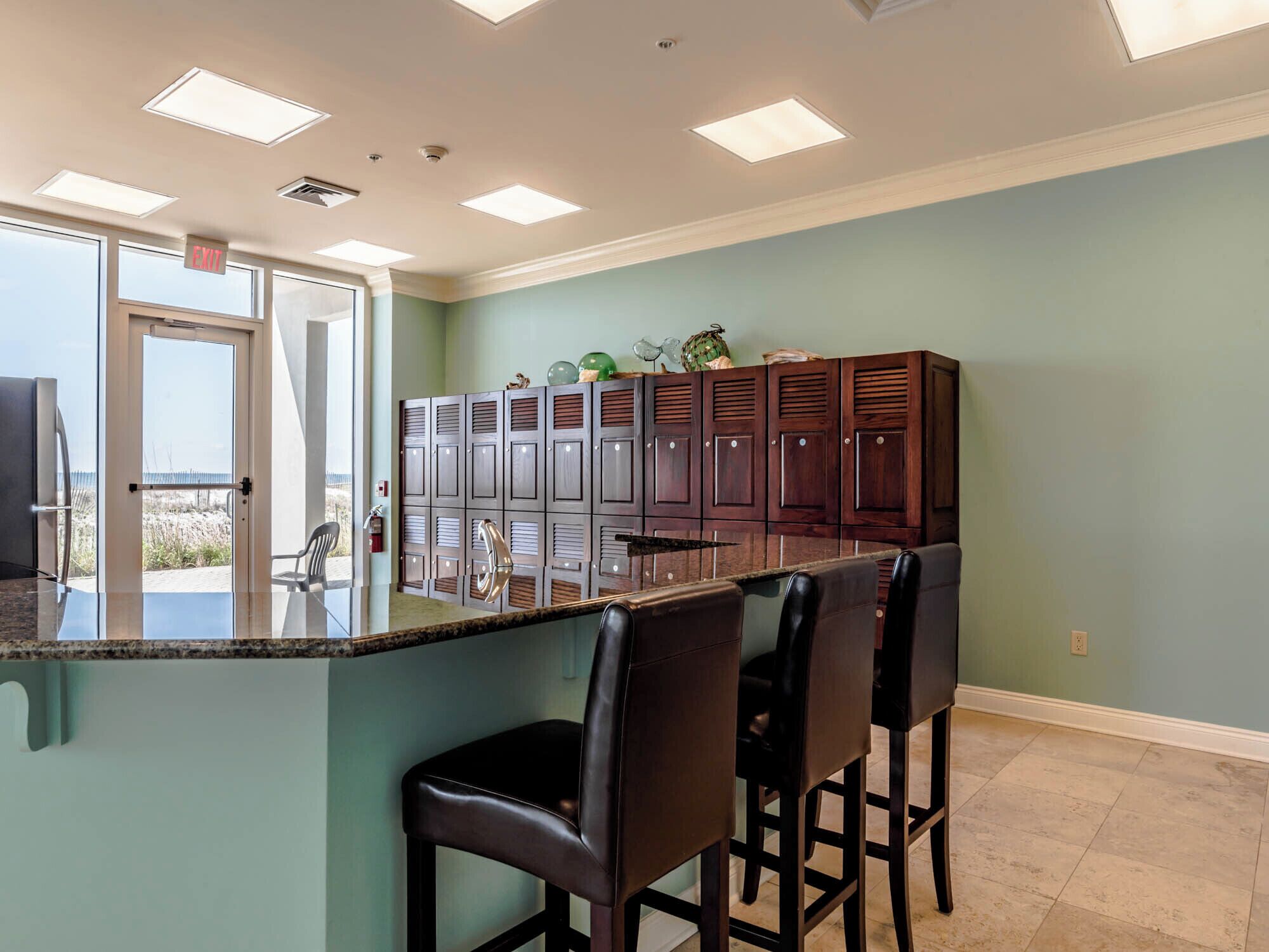 A kitchen with a central island, bar stools, and a view through the glass door.