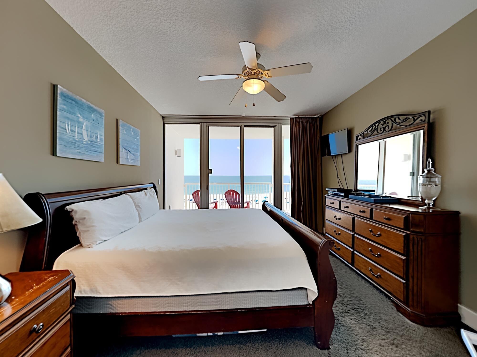 Ein Hotelzimmer mit einem Bett, einem Schminktisch, einem Deckenventilator, einem Fernseher und einem Balkon mit Meerblick.