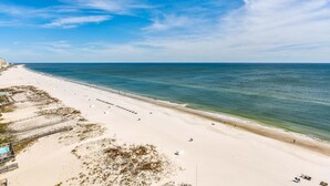 A beach with a clear sky, sandy shore, and a few buildings in the background. - Island Towers by Southern Vacation Rentals (Gulf Shores)