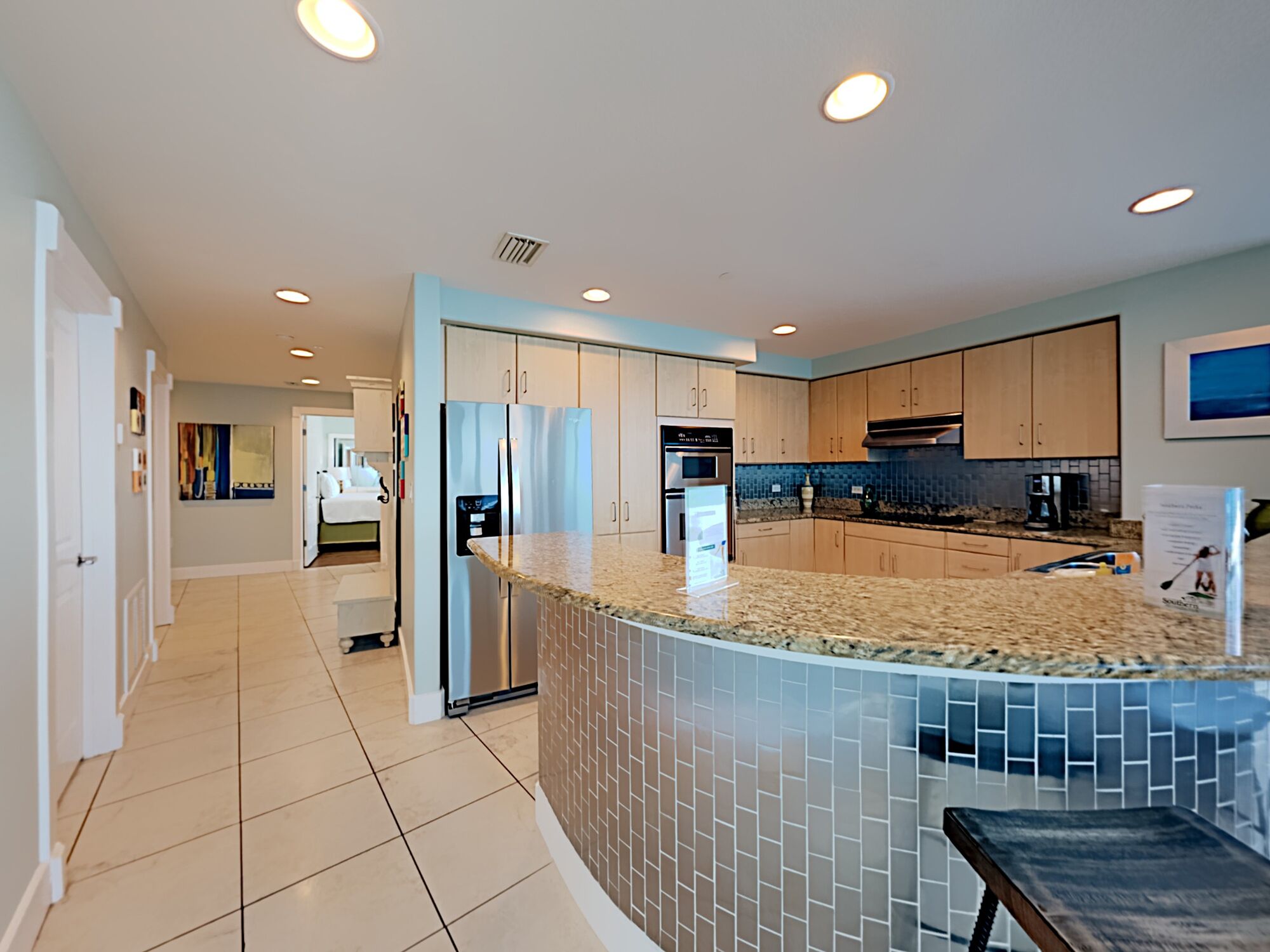 A modern kitchen with a curved island, stainless steel appliances, and a tiled backsplash.