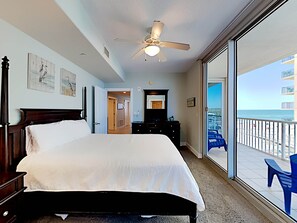 A bedroom with a large bed, a ceiling fan, a dresser, and a view of the beach through a sliding glass door. - Island Towers by Southern Vacation Rentals (Gulf Shores)