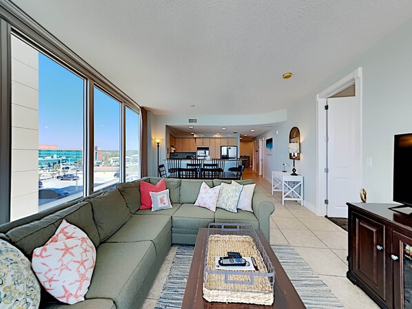 A living room with a large window, a sofa, a coffee table, and a TV. - Island Towers by Southern Vacation Rentals (Gulf Shores)