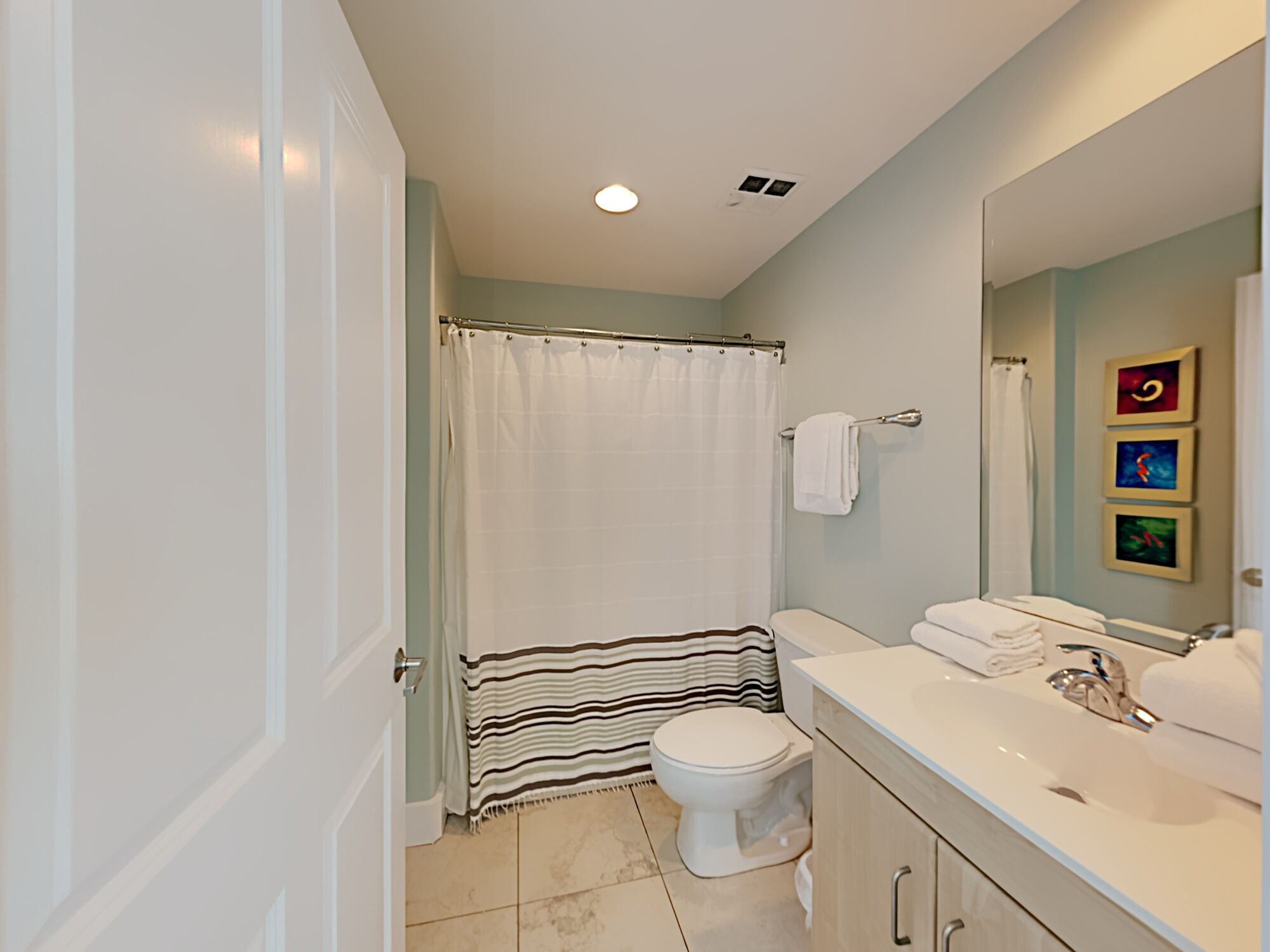 A modern bathroom with a shower curtain, a toilet, a sink with a mirror, and a towel rack.