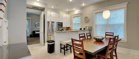 A modern kitchen with white cabinets, a built-in oven, and a dining area with a wooden table and chairs.