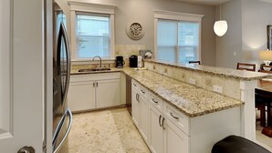 A modern kitchen with white cabinets, granite countertops, a built-in oven, and a clock on the wall. - Miramar Beach Villas by Southern Vacation Rentals (Miramar Beach)