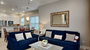 A modern living room with two blue sofas, a coffee table, and a dining area with wooden chairs and a table. - Miramar Beach Villas by Southern Vacation Rentals (Miramar Beach)