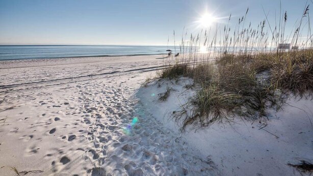 A sandy beach with footprints leading to the water, a clear sky, and the sun shining. - Miramar Beach Villas by Southern Vacation Rentals (Miramar Beach)