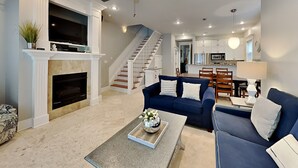 A spacious living room with a fireplace, a blue sofa, a coffee table with a decorative tray, and a staircase leading to the upper floor. - Miramar Beach Villas by Southern Vacation Rentals (Miramar Beach)