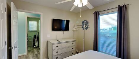 A bedroom with a bed, a ceiling fan, a TV, a dresser, and a window with curtains.