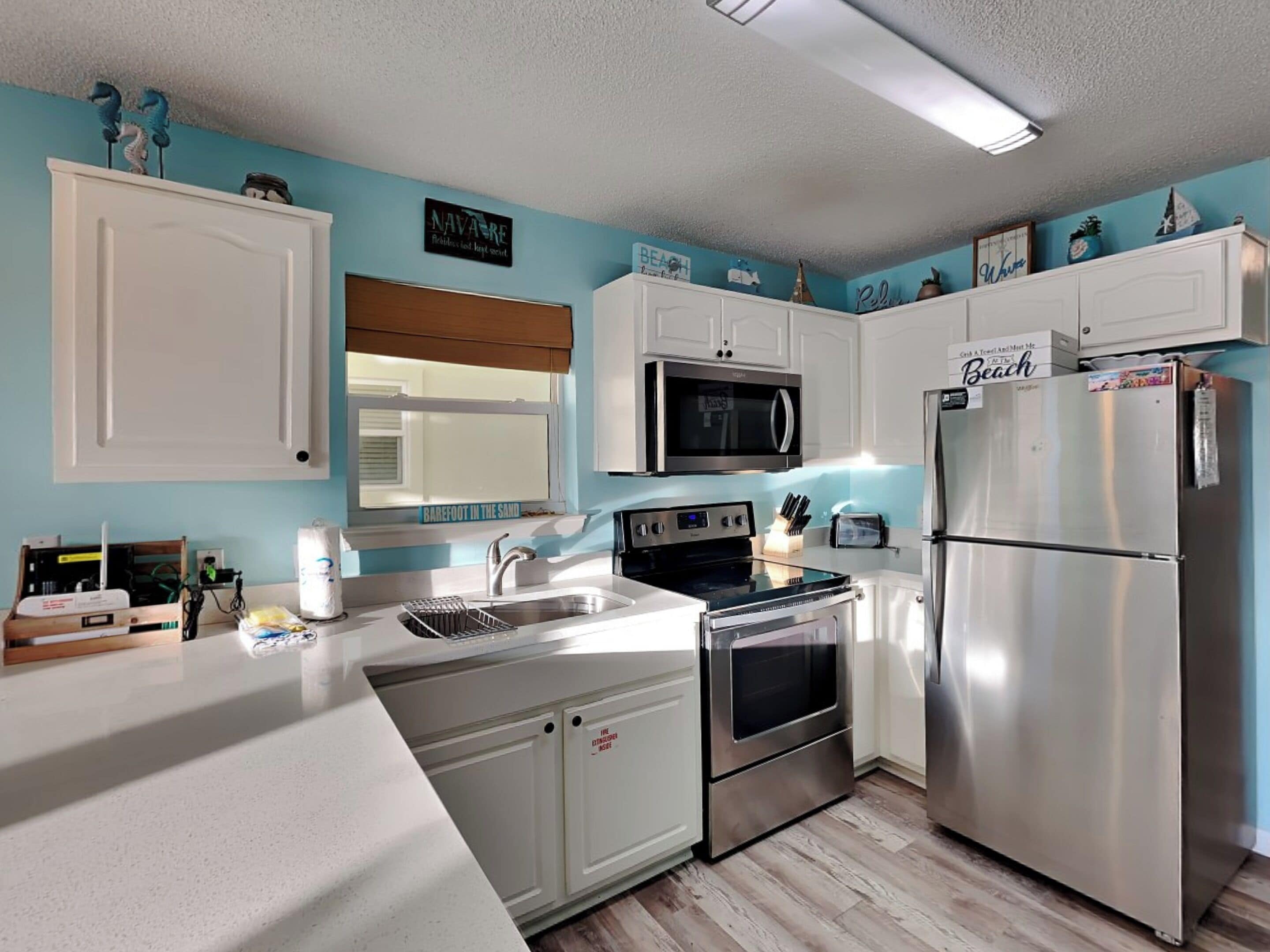 Una cocina moderna con armarios blancos, electrodomésticos de acero inoxidable y objetos decorativos en las paredes.