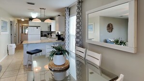 A modern kitchen with white cabinets, a central island, pendant lighting, and a dining area with a glass table and chairs. - Gulf Island by Southern Vacation Rentals (Navarre)