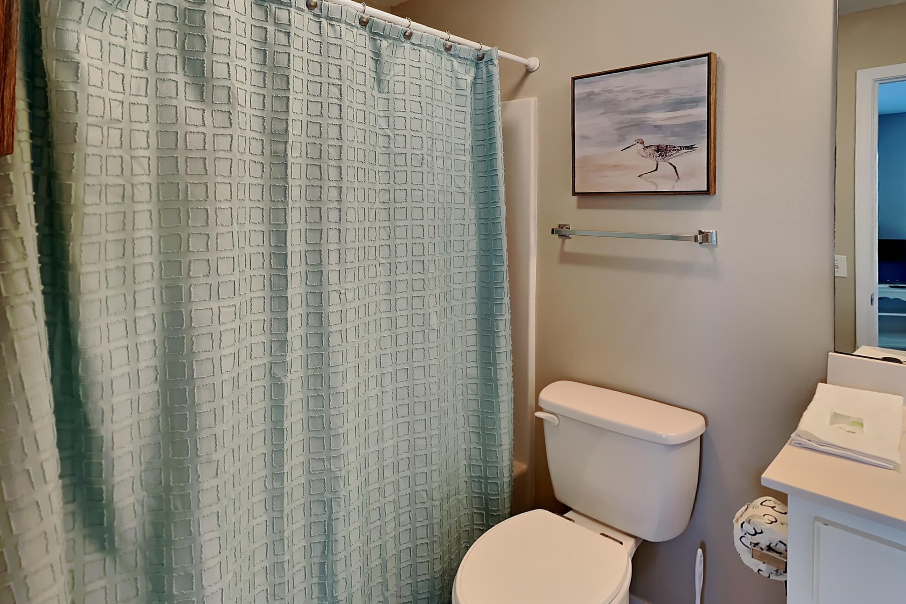 Et badeværelse med bruseforhæng, toilet og et billede i ramme.