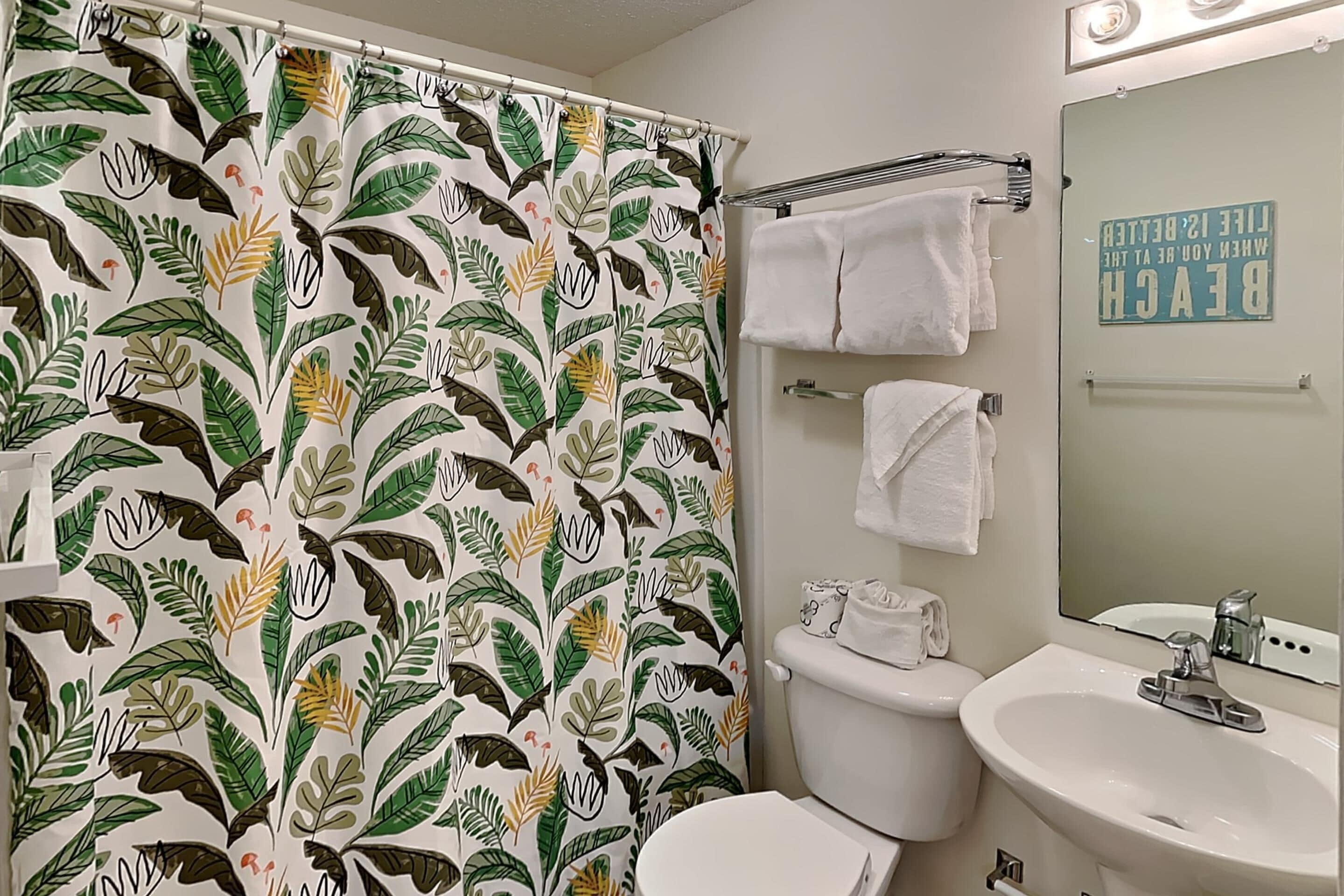 A bathroom with a shower curtain featuring a leaf pattern, a toilet, a sink, and a towel rack.