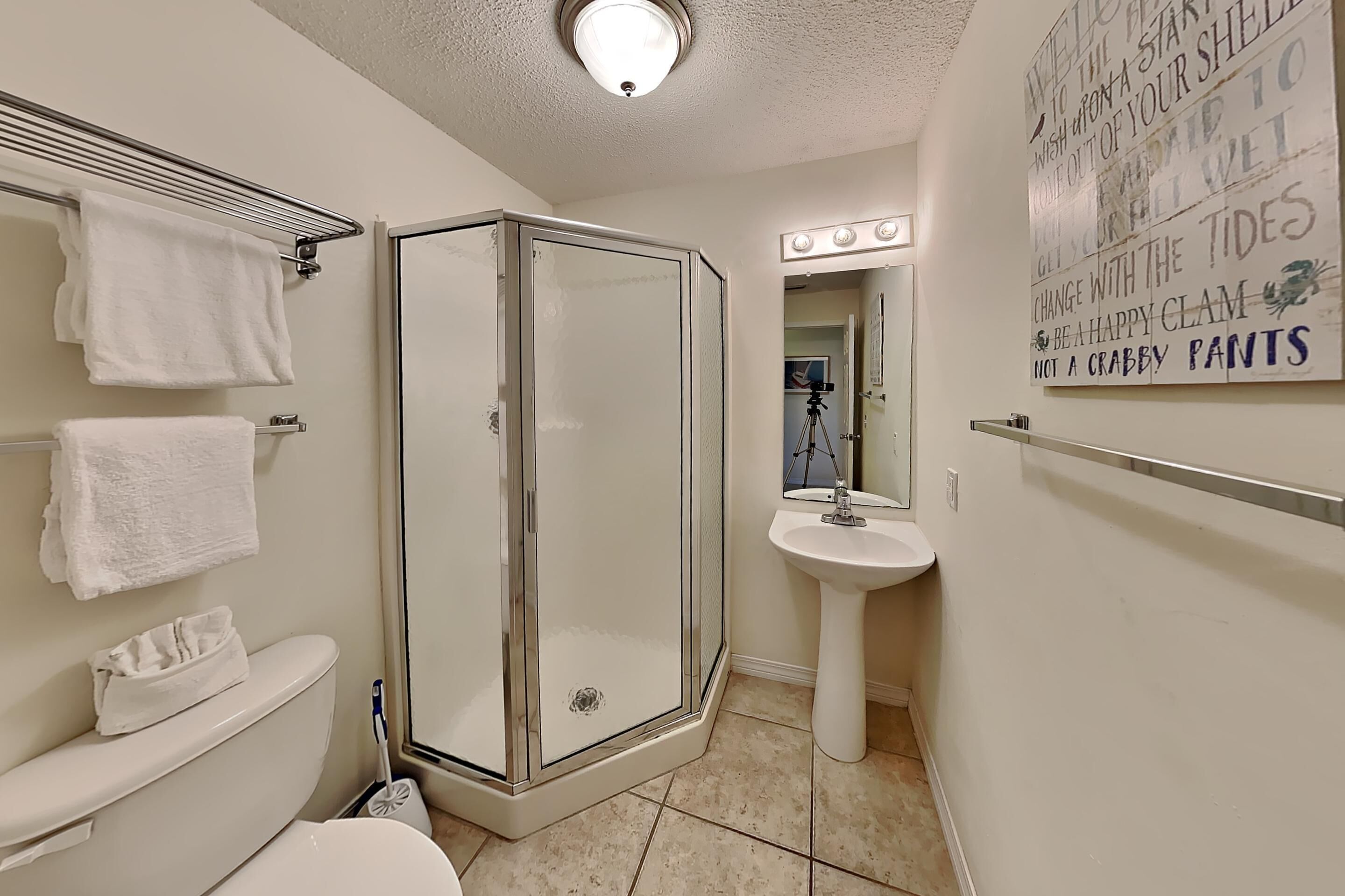 A bathroom with a glass-enclosed shower, a toilet, a sink, and a mirror with lights above it.