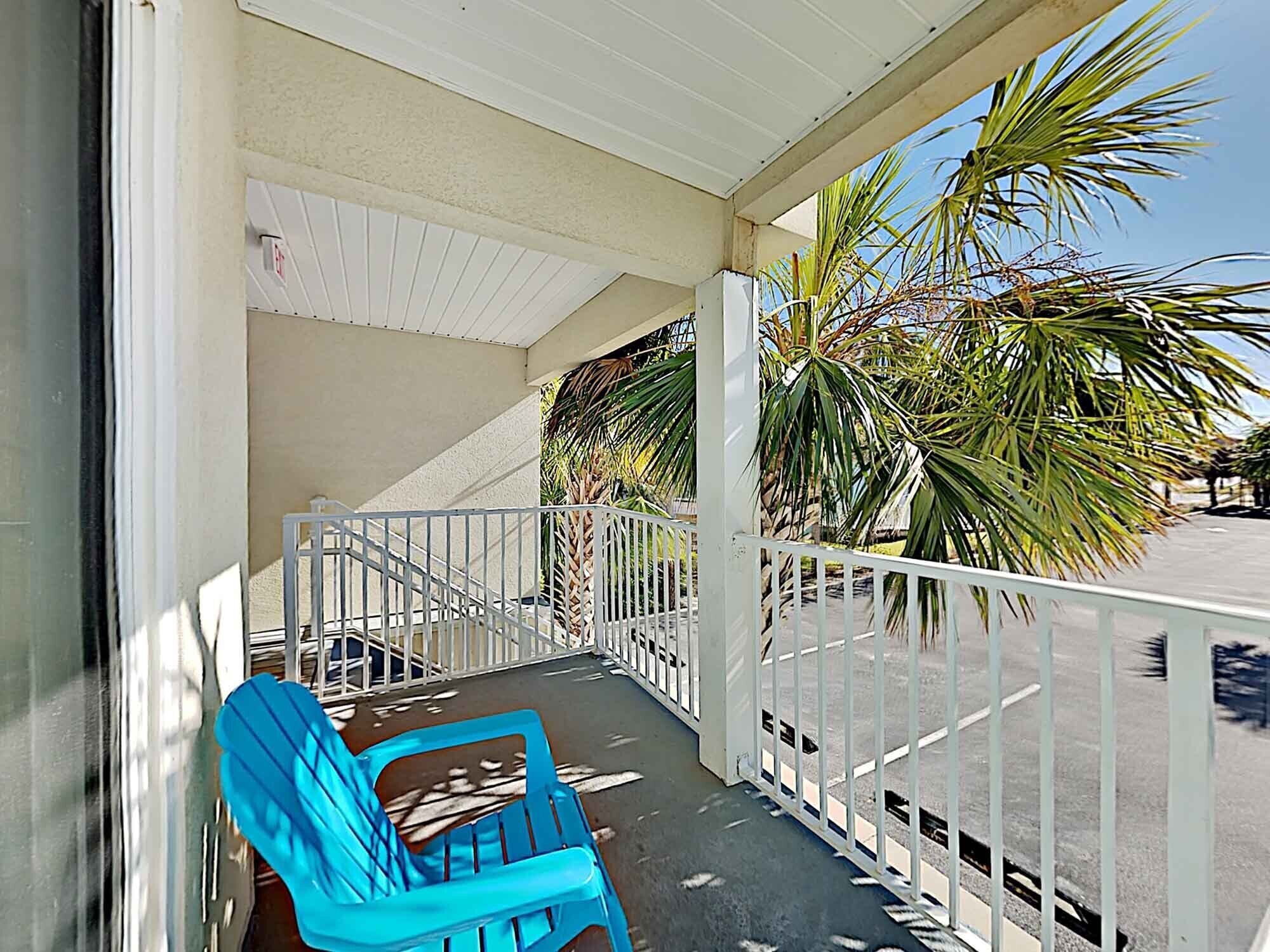 A covered outdoor area with a blue chair, white railing, and palm trees.
