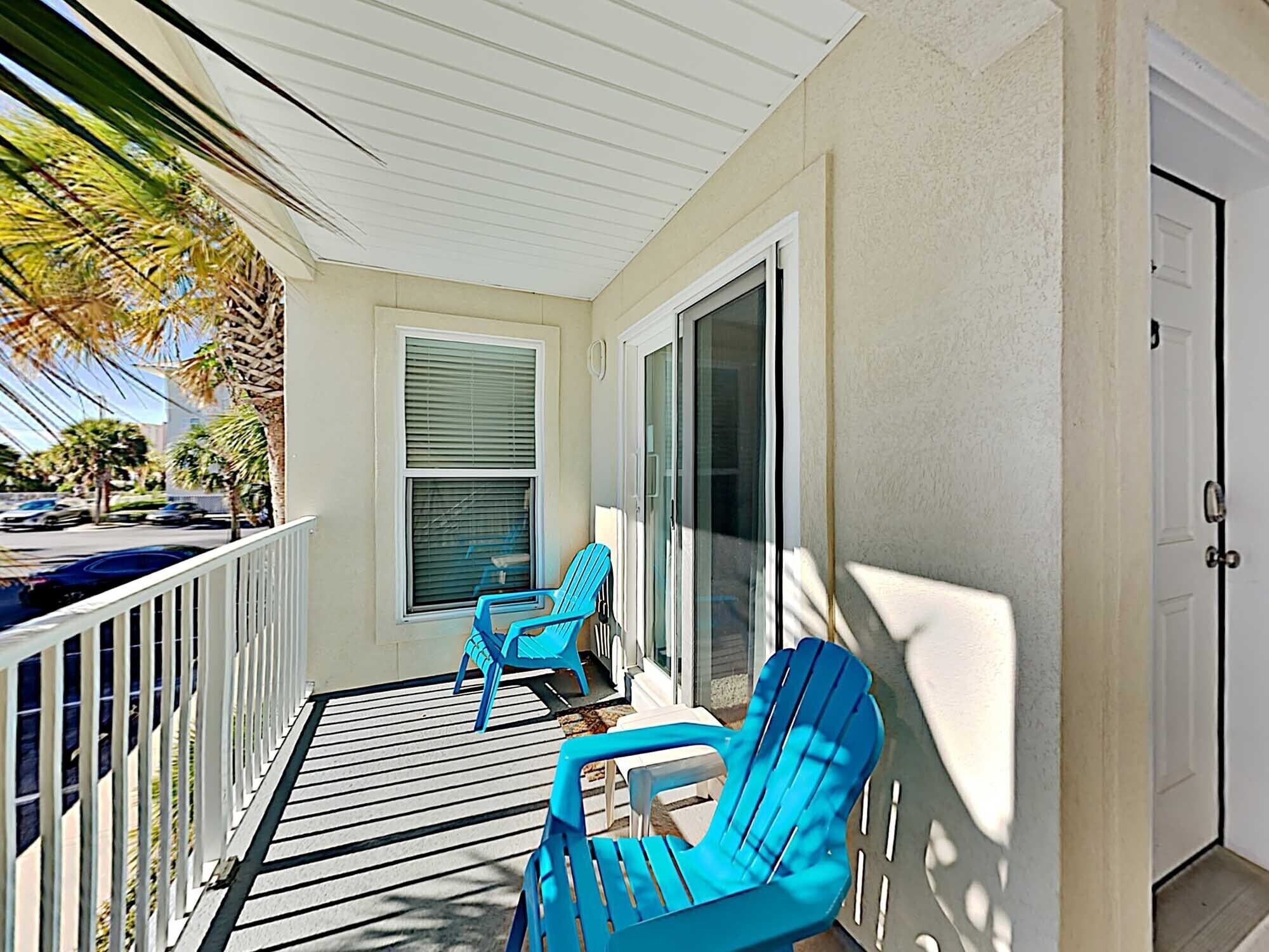 A covered porch with two blue chairs, a window with blinds, and a door.