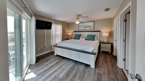 A bedroom with a large bed, a ceiling fan, a TV mounted on the wall, and a sliding glass door leading to an outdoor area. - Gulf Island by Southern Vacation Rentals (Navarre)