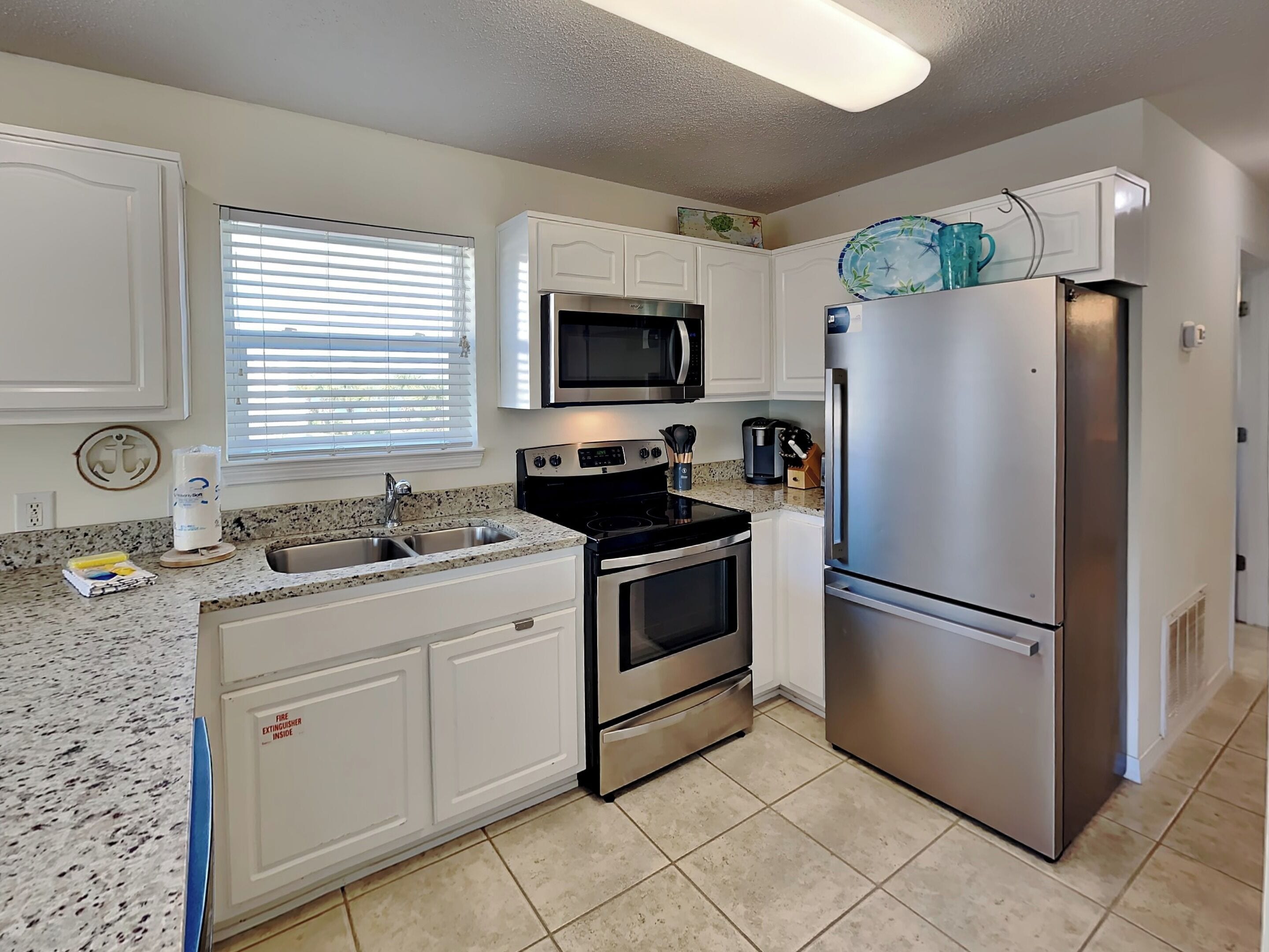 A modern kitchen with white cabinets, stainless steel appliances, a granite countertop, and a window with blinds.